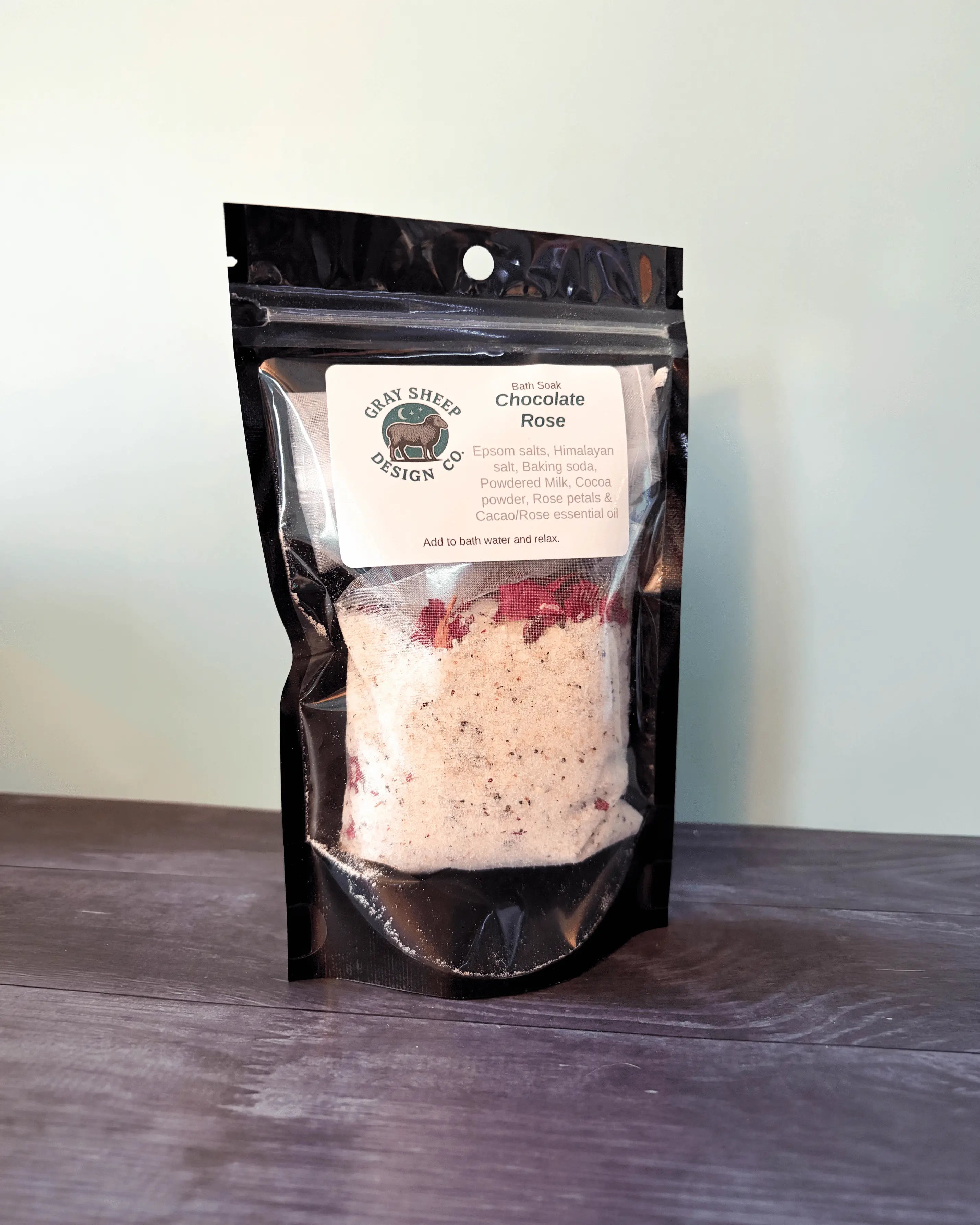 Chocolate Rose bath soak in a resealable black pouch, cocoa-flecked salts and rose petals visible through the window.