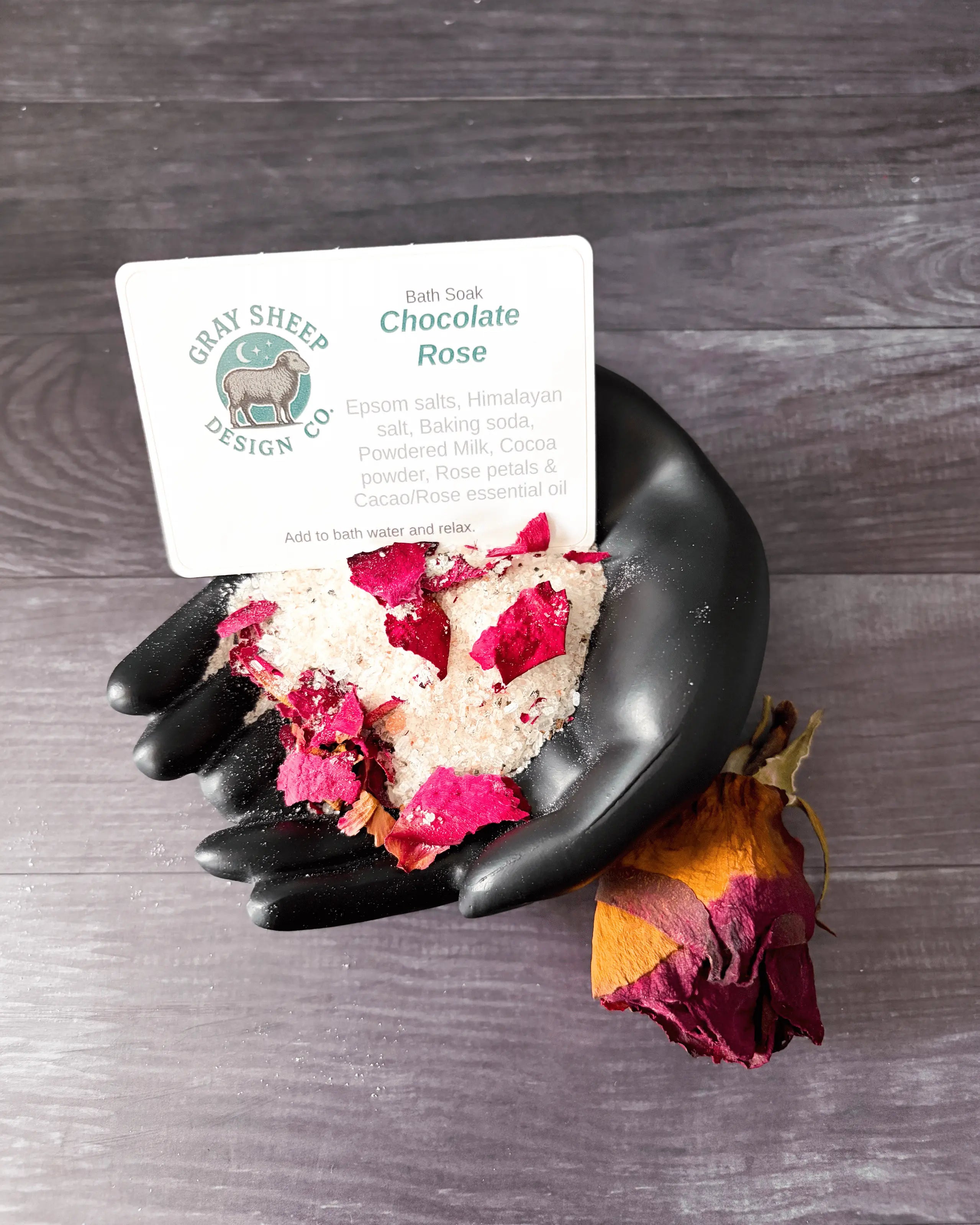Loose Chocolate Rose soak in a black hand-shaped dish — cocoa-dusted salts, rose petals, and a dried rose.