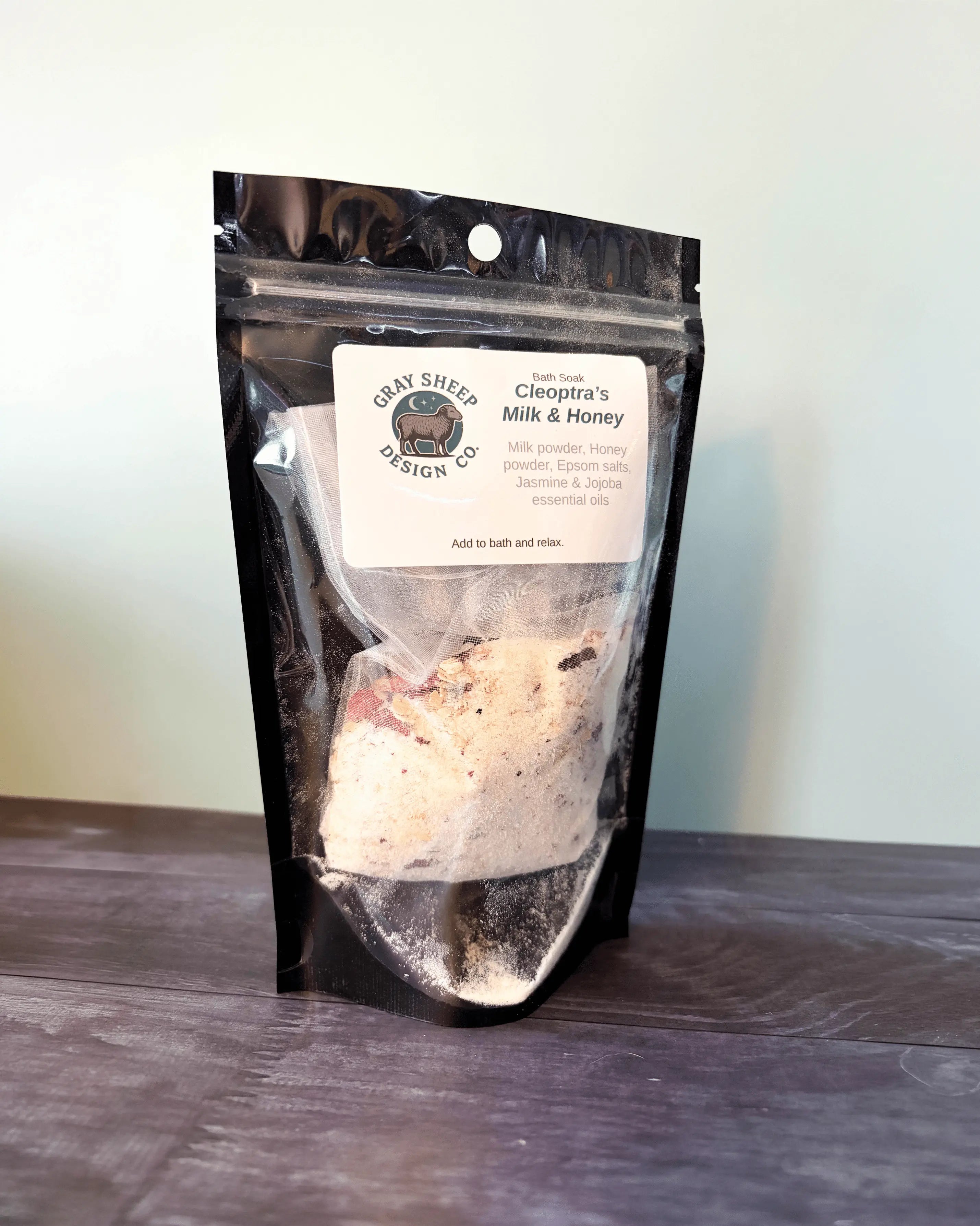 Cleopatra's Milk & Honey bath soak in a resealable black pouch, creamy milk-and-honey powder visible through the window.