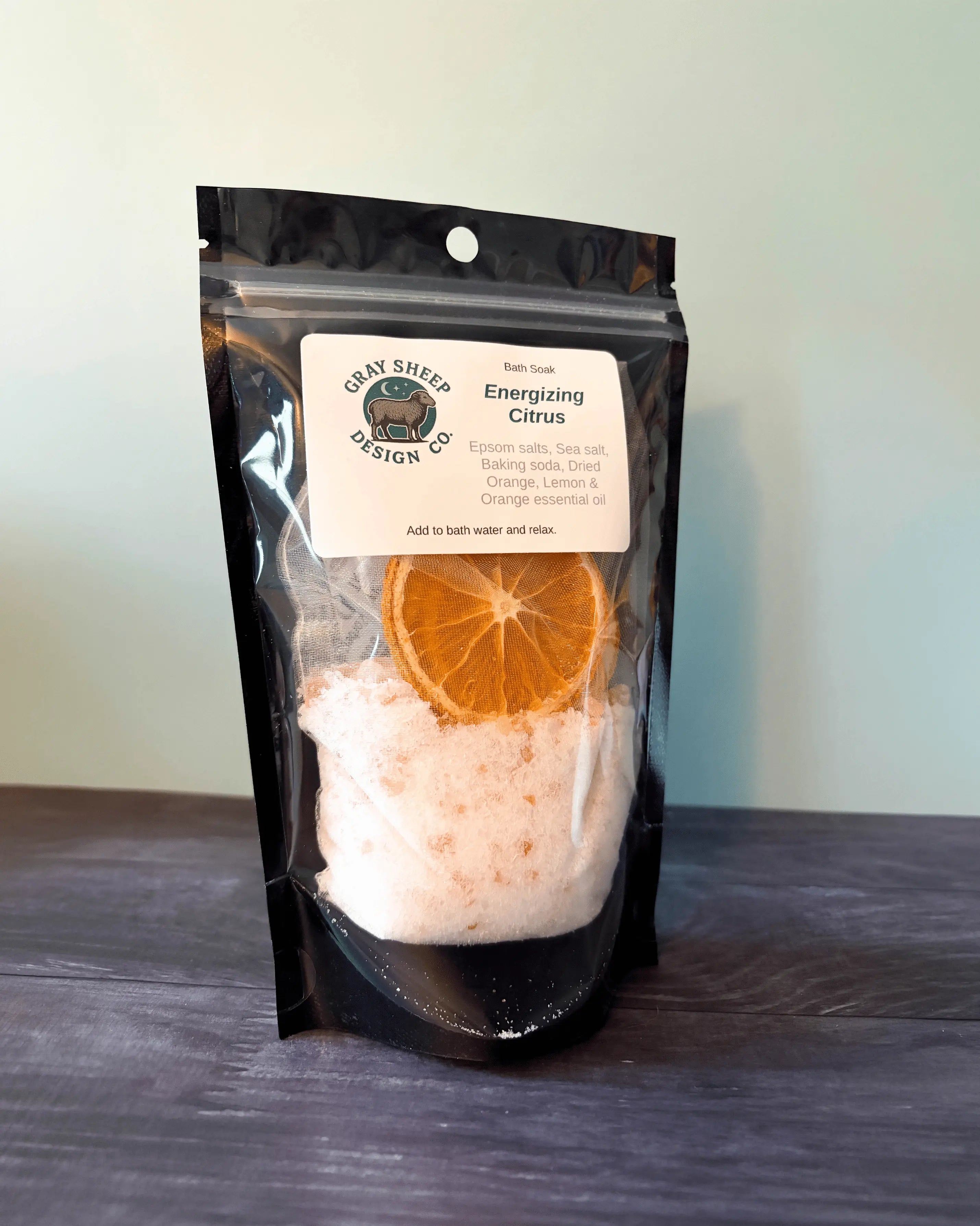 Energizing Citrus bath soak in a resealable black pouch, a dried orange slice and pale salts visible through the window.