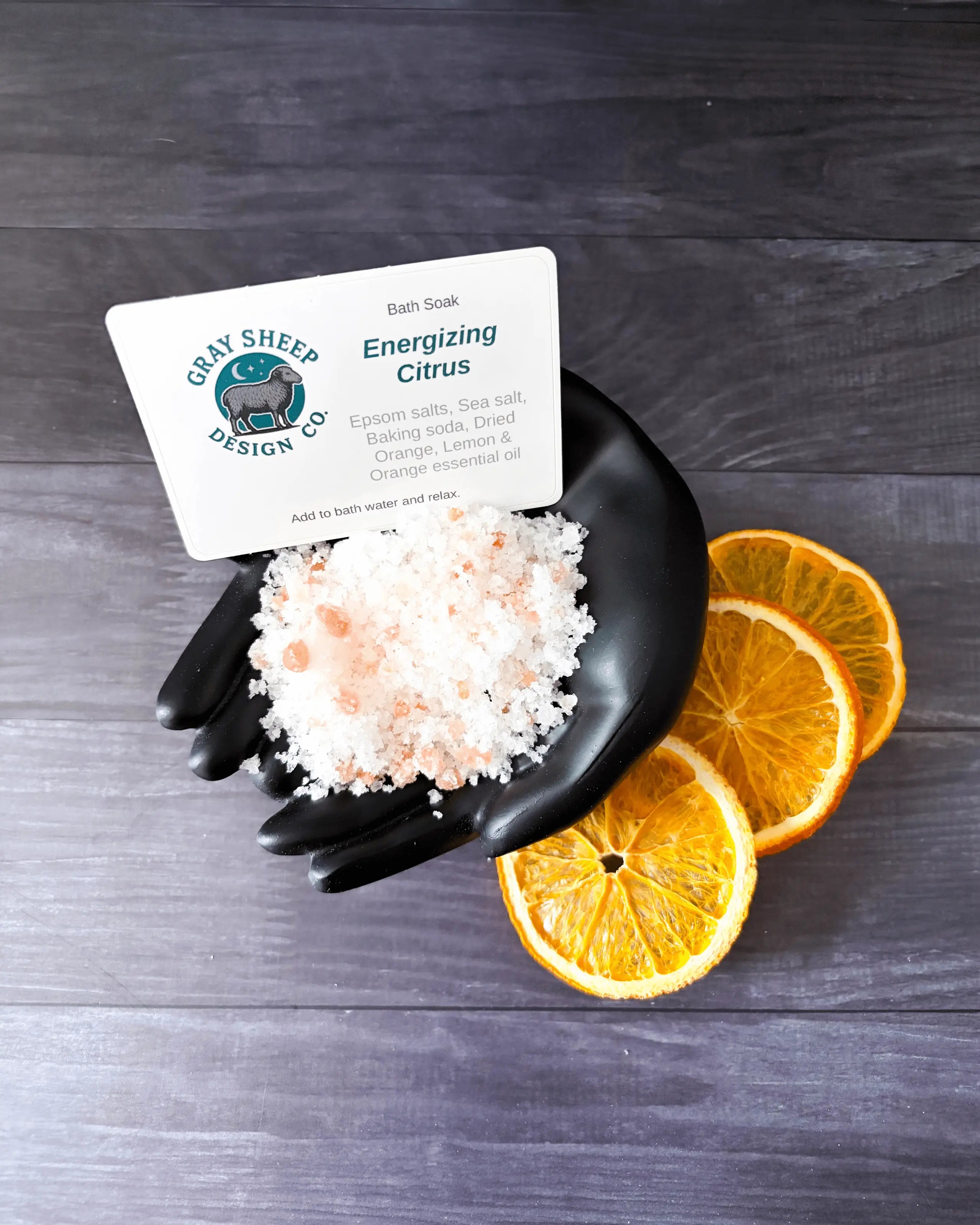 Loose Energizing Citrus soak in a black hand-shaped dish — coarse white salts with dried orange slices.