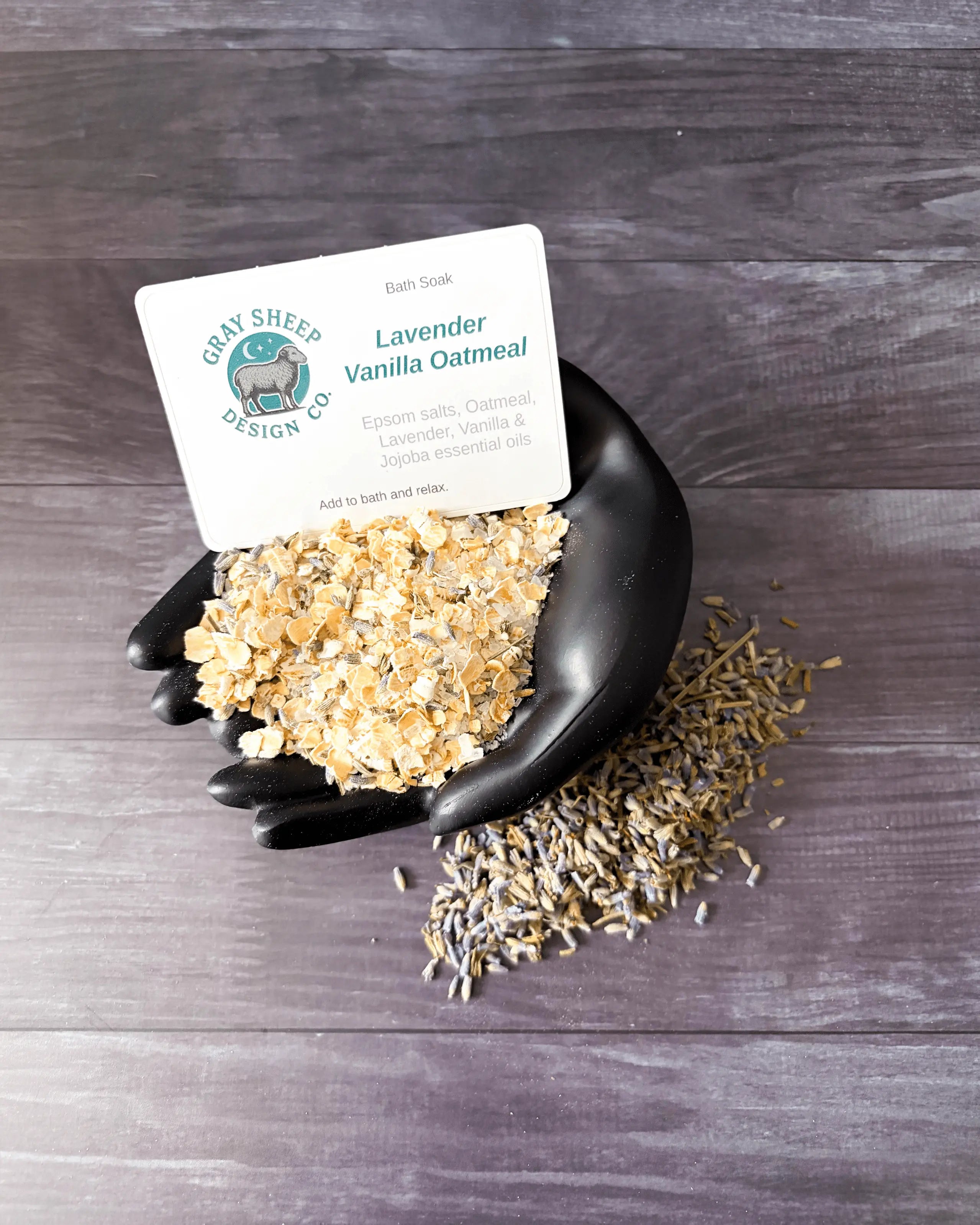 Loose Lavender Vanilla Oatmeal soak in a black hand-shaped dish — oat flakes and salts with dried lavender.