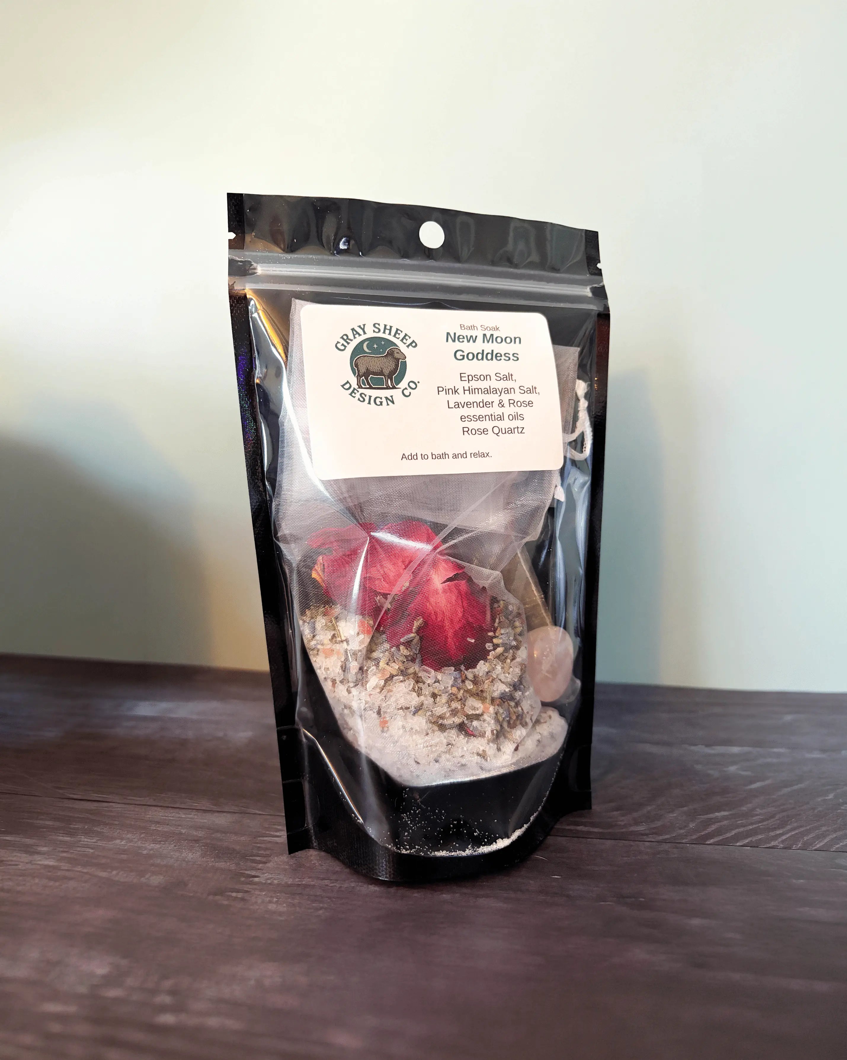 New Moon Goddess bath soak in a resealable black pouch, a dried rose and rose quartz stone visible inside.