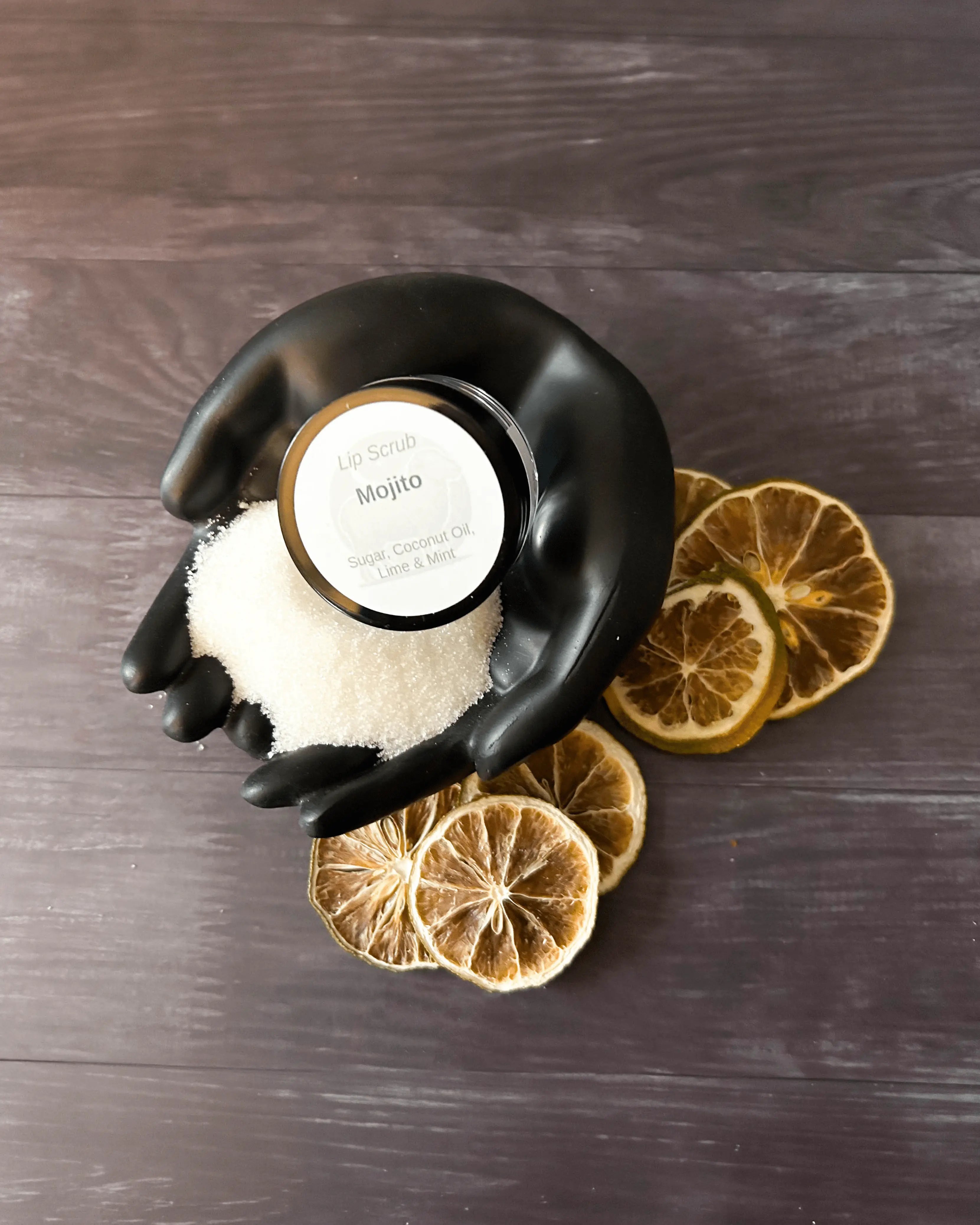Open jar of Mojito lip scrub in a black hand-shaped dish with dried lime slices.