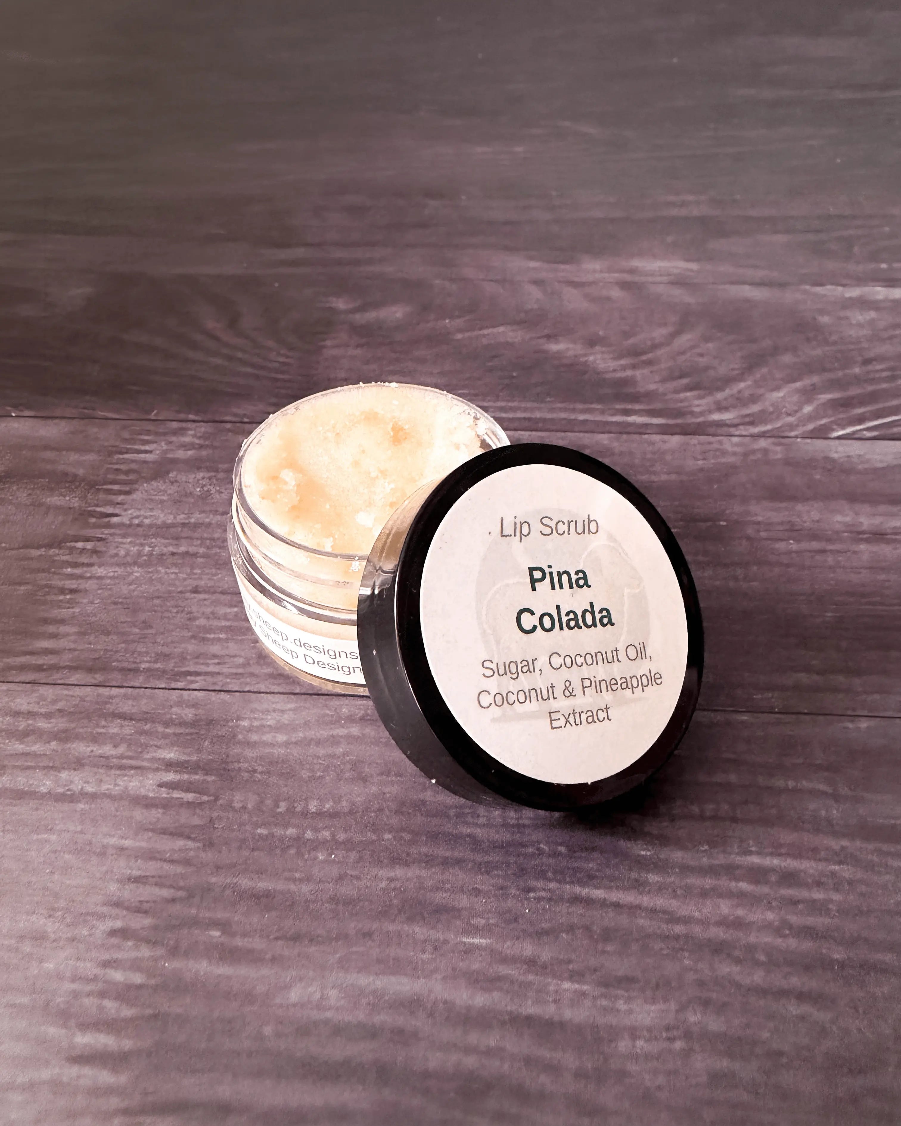 Piña Colada lip scrub in a small clear jar with a black lid, creamy sugar scrub inside.
