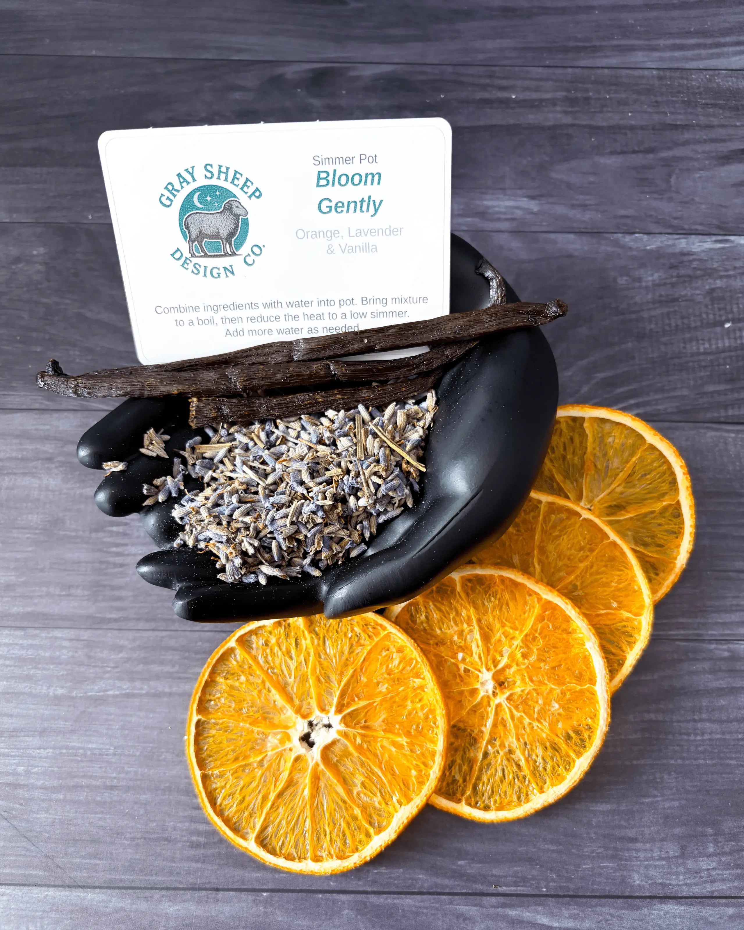 Loose Bloom Gently blend in a black hand-shaped dish — lavender, vanilla beans, and dried orange slices.