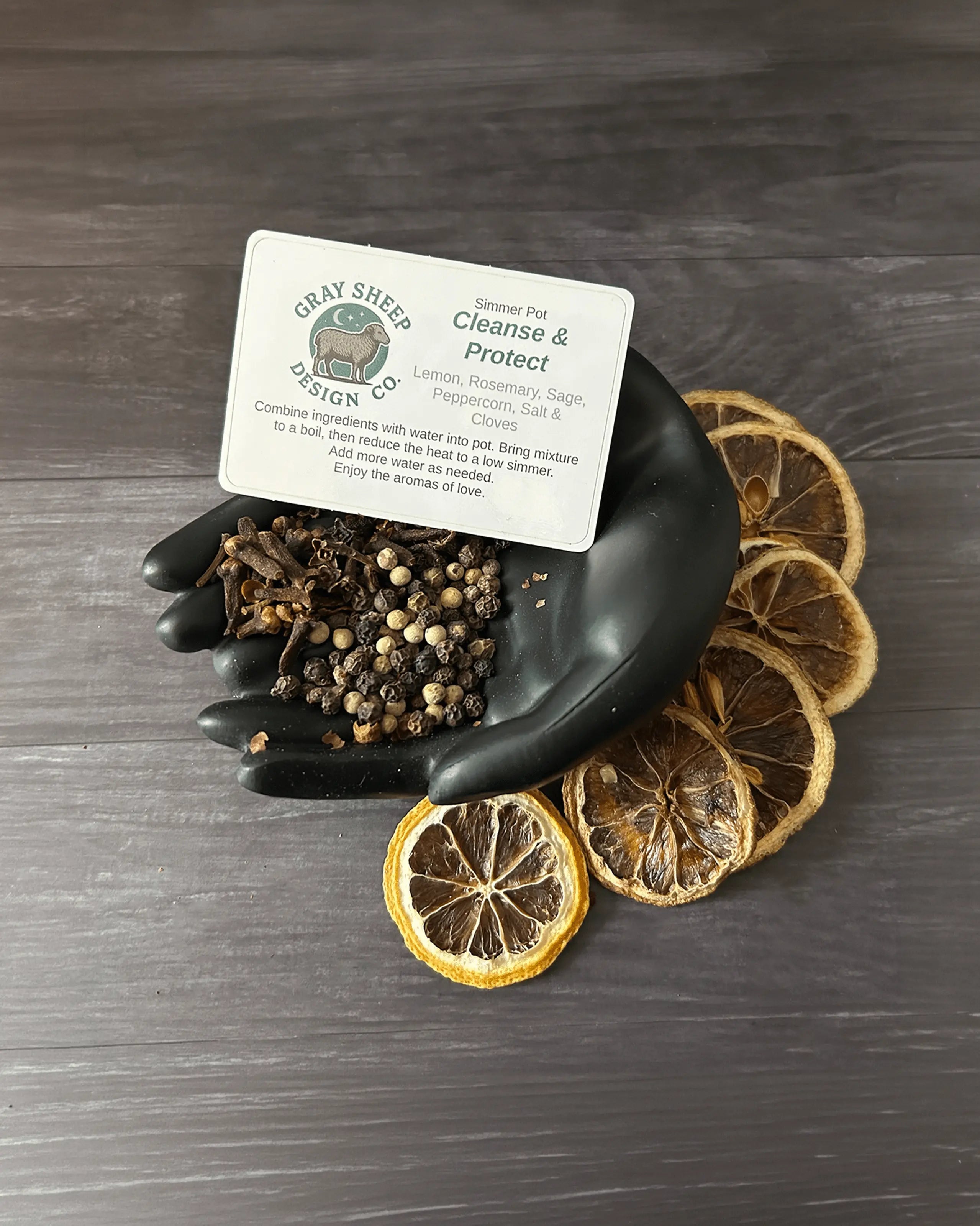 Loose Cleanse & Protect blend in a black hand-shaped dish — peppercorns, dried herbs, and lemon slices.