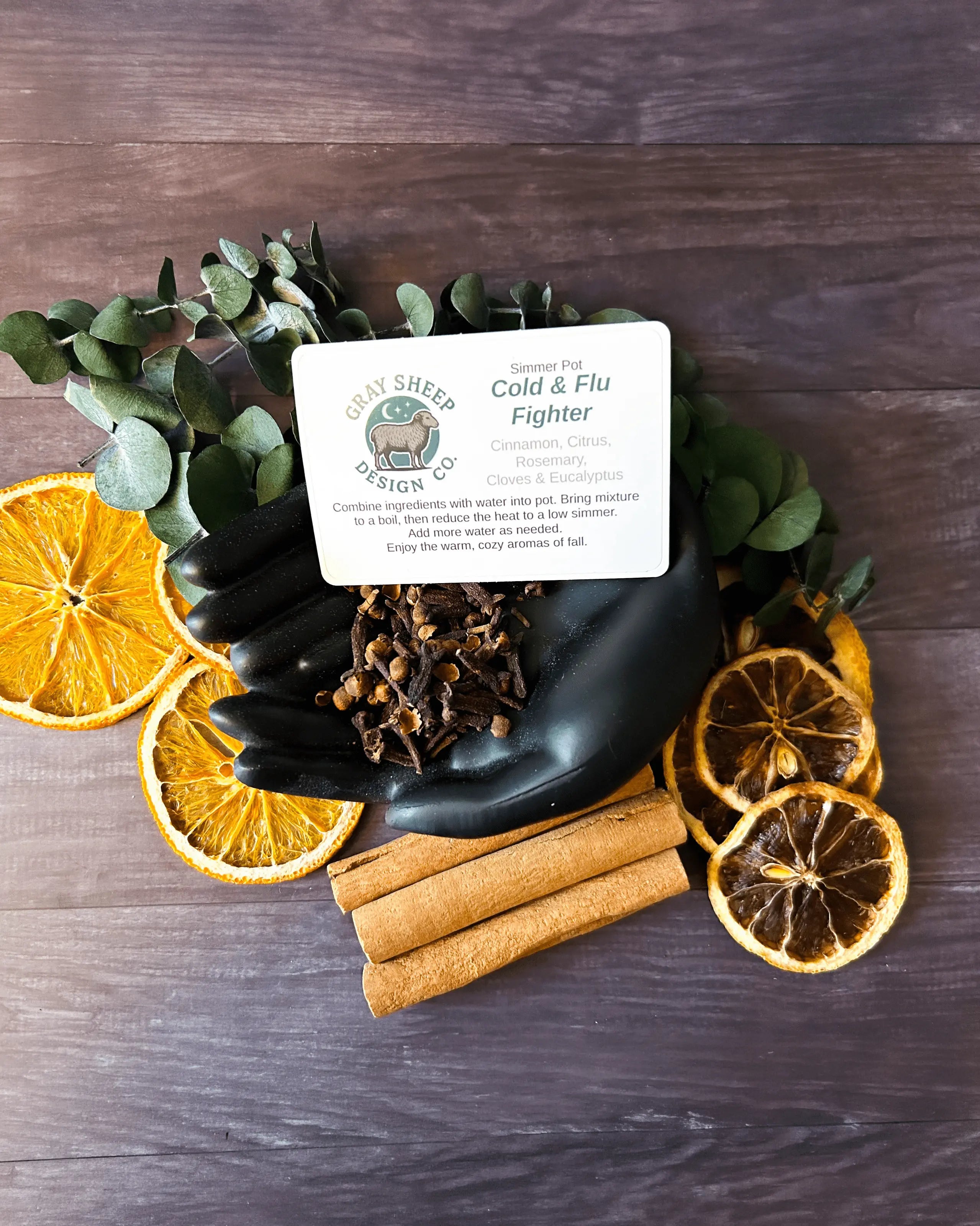 Loose Cold & Flu Fighter blend in a black hand-shaped dish — eucalyptus, dried orange and lemon slices, and cinnamon sticks.