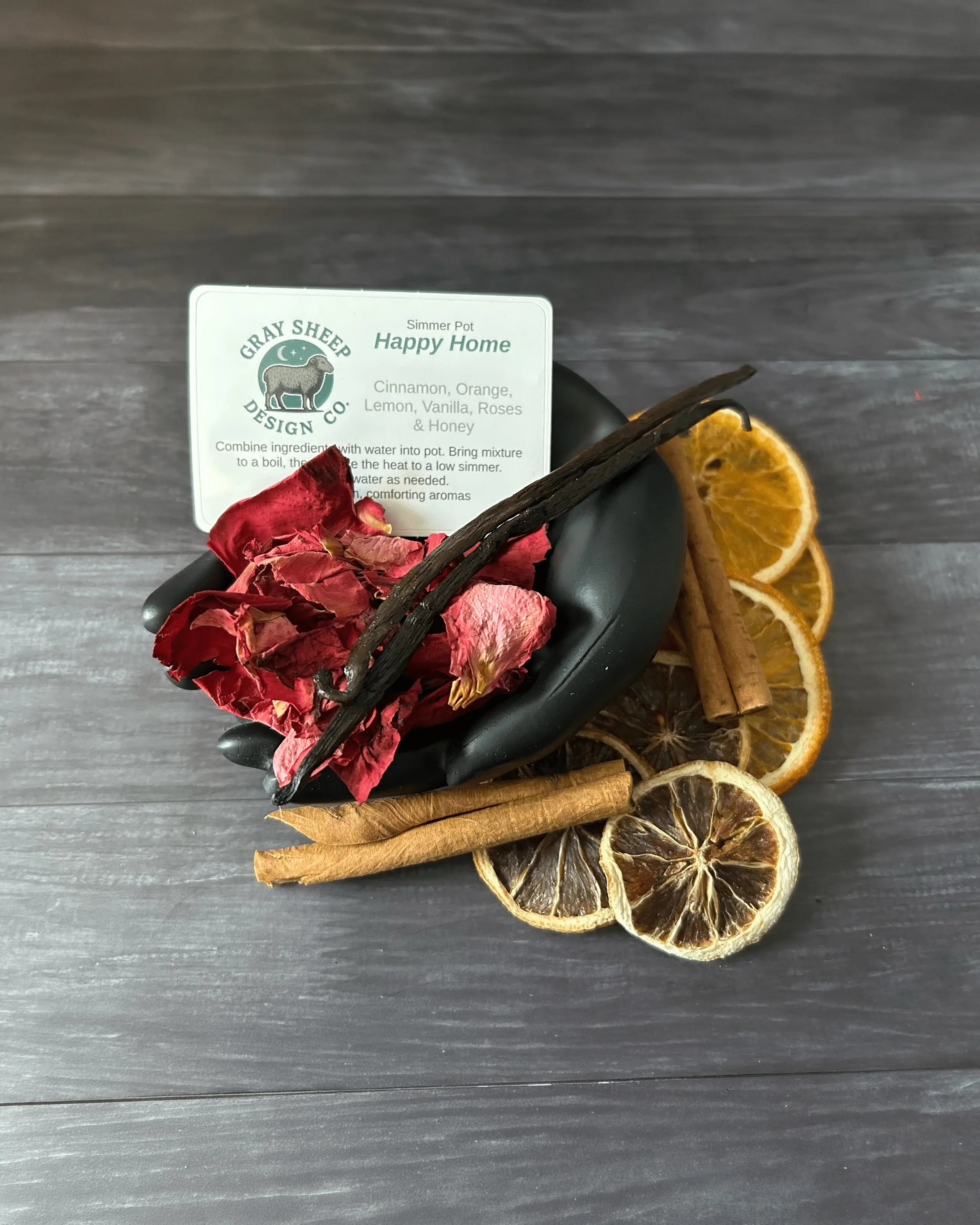 Loose Happy Home blend in a black hand-shaped dish — rose petals, cinnamon sticks, vanilla, and dried citrus slices.