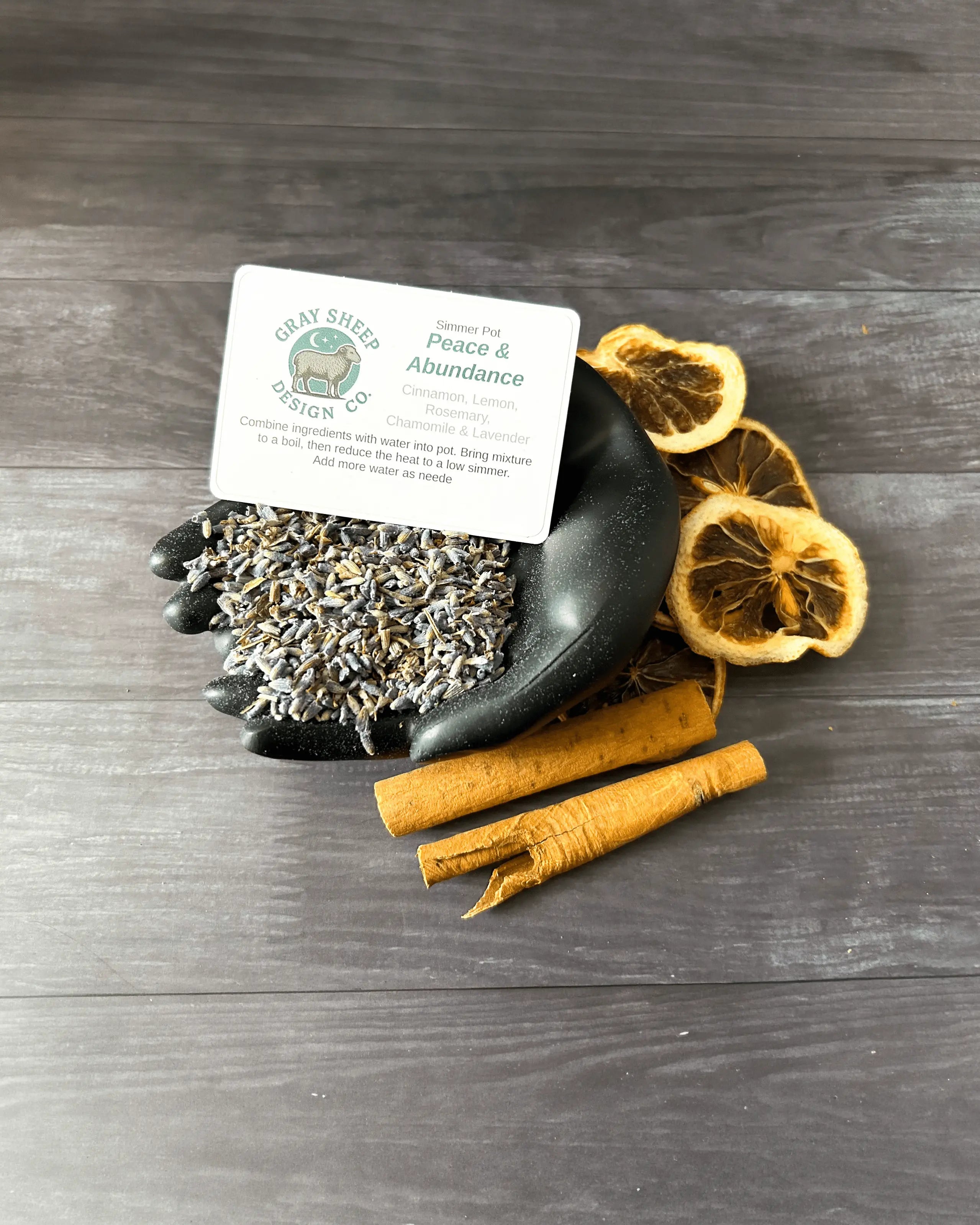Loose Peace & Abundance blend in a black hand-shaped dish — lavender, dried lemon slices, and cinnamon sticks.