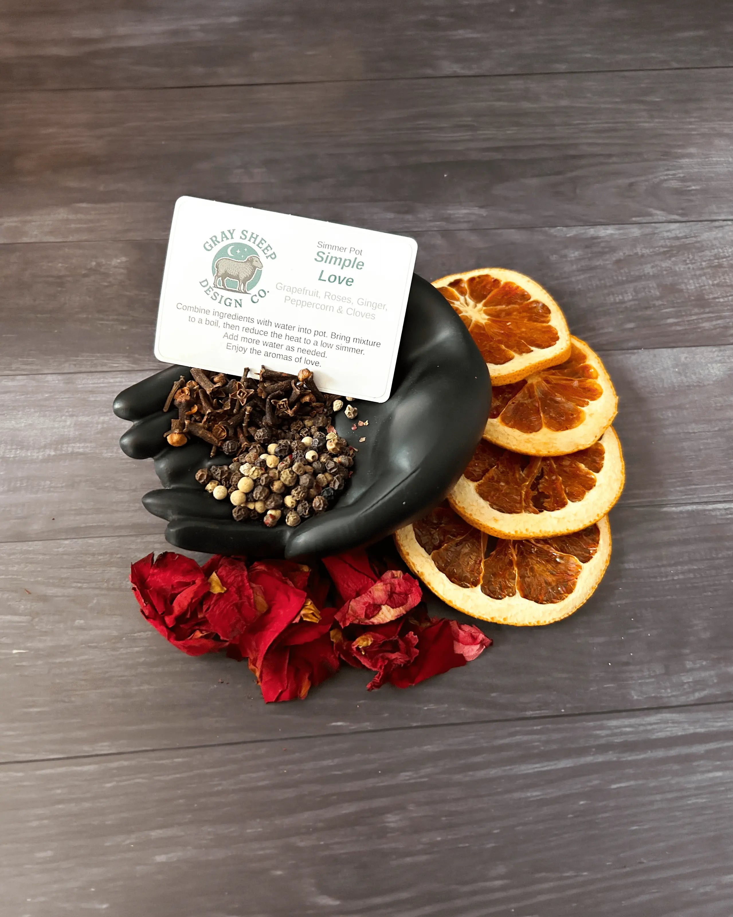 Loose Simple Love blend in a black hand-shaped dish — peppercorns, dried grapefruit slices, and red rose petals.