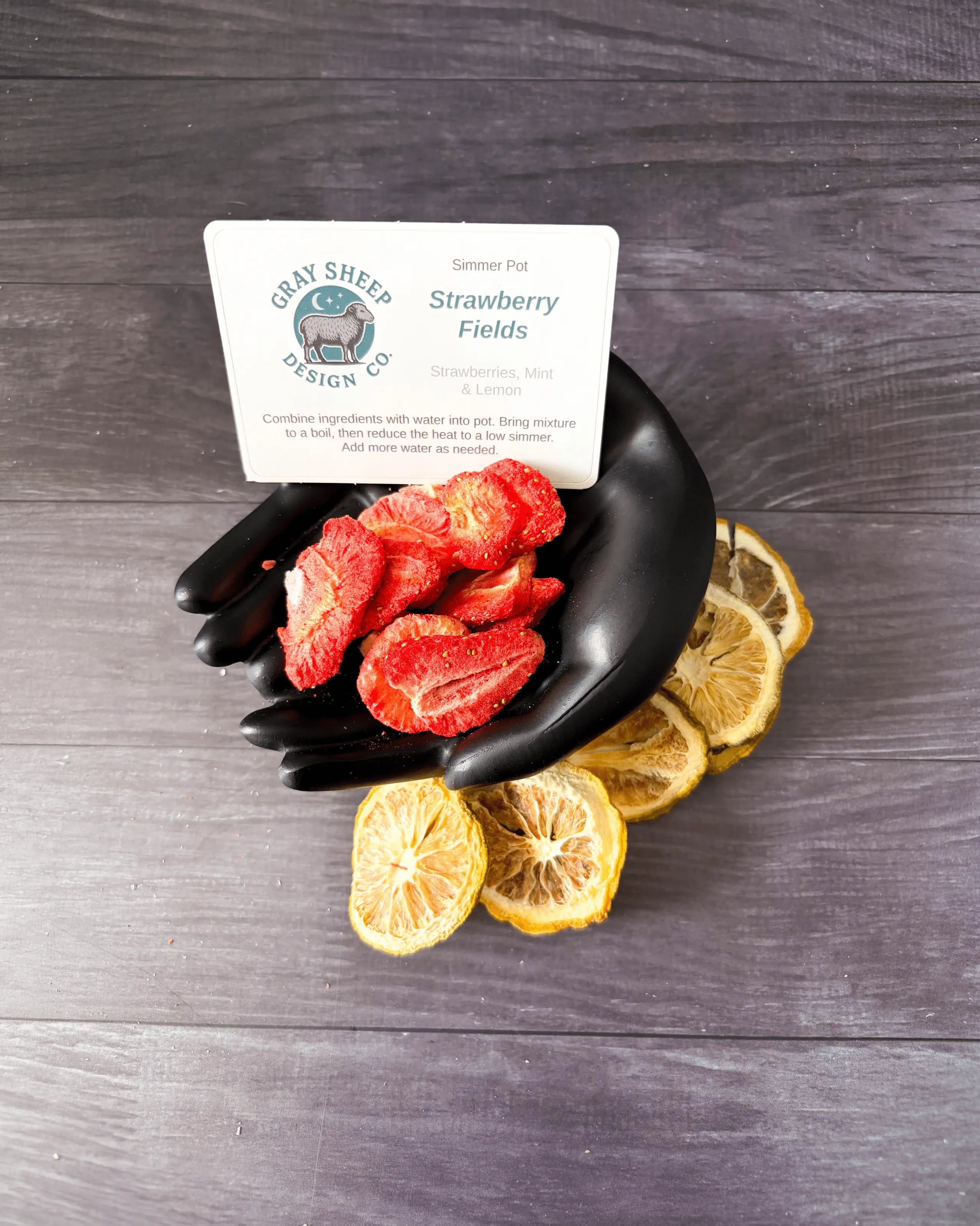 Loose Strawberry Fields blend in a black hand-shaped dish — dried strawberries and lemon slices.