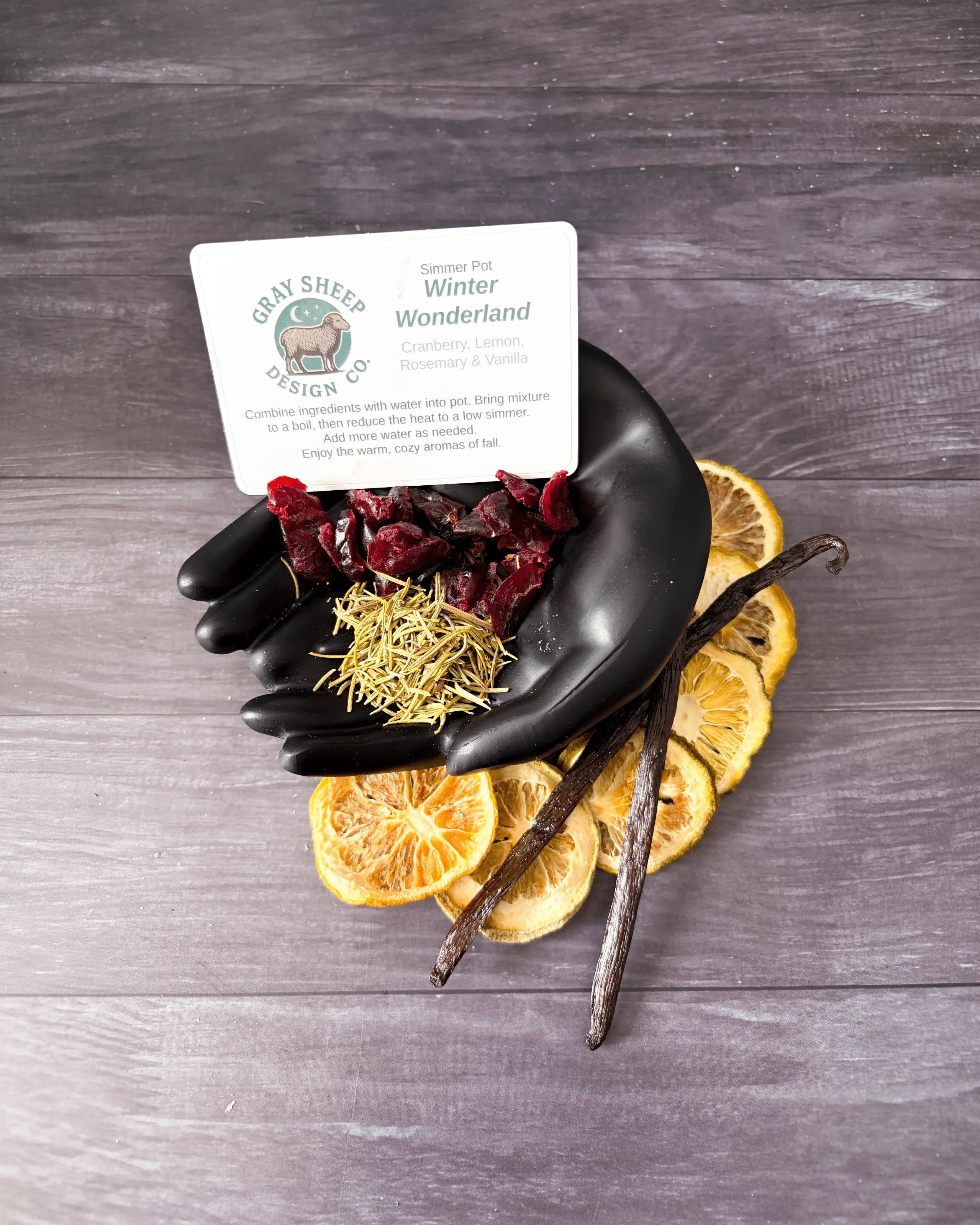 Loose Winter Wonderland blend in a black hand-shaped dish — dried cranberries, rosemary, lemon slices, and vanilla beans.